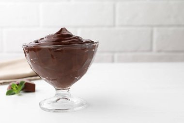 Tatlı kasesindeki çikolatalı puding beyaz masada tuğla duvara karşı, yakın plan. Metin için boşluk