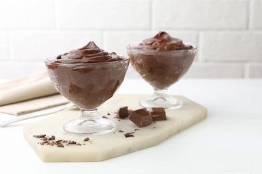 Tatlı kaselerinde lezzetli çikolatalı puding beyaz masada tuğla duvara karşı, yakın plan.