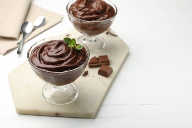 Beyaz ahşap masadaki tatlı kaselerinde lezzetli çikolatalı puding, yakın plan. Metin için boşluk