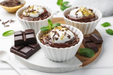 Krem şantili lezzetli puding ve beyaz ahşap masadaki çikolata parçaları, yakın plan.