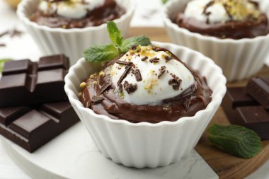 Lezzetli puding, krem şantili ve beyaz masadaki çikolata parçaları, yakın plan.