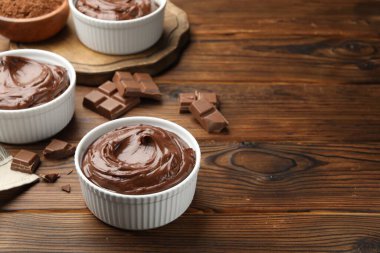 Tabaklardaki lezzetli pudingler ve ahşap masadaki çikolata parçaları, metin için yer.