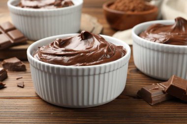 Tabaklardaki lezzetli pudingler ve ahşap masadaki çikolata parçaları, yakın plan.