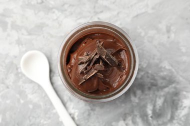 Cam kavanozda çikolatalı puding ve açık gri masada kaşık.