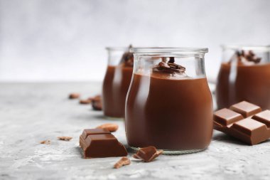 Cam kavanozlarda lezzetli puding ve açık gri masada çikolata parçaları, yakın plan. Metin için boşluk