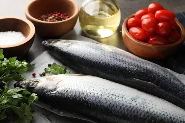 Gri masada tuzlu ringa balıkları, baharatlar ve domatesler, yakın plan.