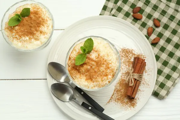 Tarçınlı, nane, badem ve kaşıklı lezzetli sütlaç beyaz ahşap masa, düz uzanmış