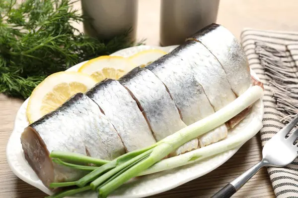 Limon dilimli lezzetli ringa balıkları, yeşil soğan ve ahşap masada dereotu, yakın plan.