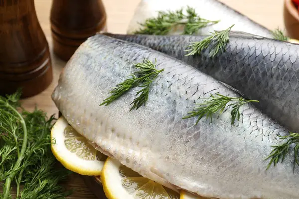 Ahşap masada dereotu ve limon dilimli lezzetli ringa filetoları, yakın plan.