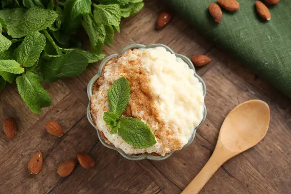 Tarçınlı, naneli, bademli ve tahta masadaki kaşıklı lezzetli sütlaç.