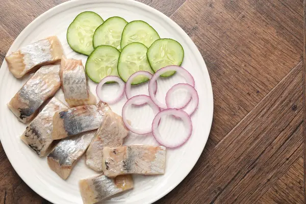 Lezzetli ringa balıkları, soğan ve ahşap masa üzerindeki salatalık dilimleri, üst manzara. Metin için boşluk