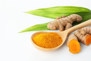 Kaşıkta zerdeçal tozu, beyaz arka planda yeşil yapraklar ve kökler, yakın plan. Metin için boşluk