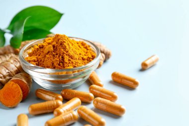 Açık mavi arka planda zerdeçal kapsülleri, toz, kökler ve yeşil yapraklar, yakın plan. Metin için boşluk