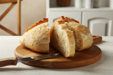 Taze pişmiş ekmek ve bıçağı beyaz ahşap masada kes, yakın plan.