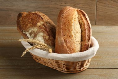 Tahta masadaki hasır sepetin içinde farklı türde taze ekmek ve çiviler, yakın plan.