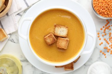 Lezzetli mercimek kremalı çorba, beyaz mermer masa üzerinde kızarmış ekmeklerle servis edilir.