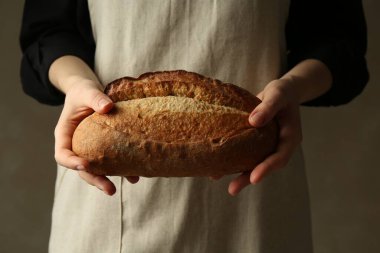 Gri arka planda taze ekmek somunu olan kadın, yakın plan.