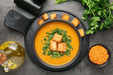 Lezzetli mercimek kremalı çorba. Gri masadaki kızarmış ekmeklerle servis ediliyor.