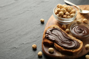 Çikolata sürülmüş bir dilim ekmek ve koyu dokulu masada fındıklar, yakın plan. Metin için boşluk