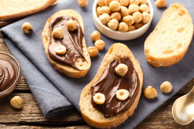 Çikolata kaplı ekmek dilimleri ve ahşap masada fındıklar.
