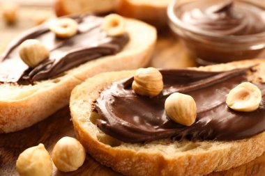 Çikolata sürülmüş ekmek dilimleri ve ahşap masada fındıklar, yakın plan.