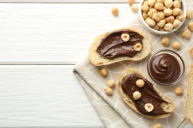 Çikolata sürülmüş ekmek dilimleri ve beyaz ahşap masada fındıklar. Metin için boşluk
