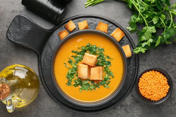 Lezzetli mercimek kremalı çorba. Gri masadaki kızarmış ekmeklerle servis ediliyor.