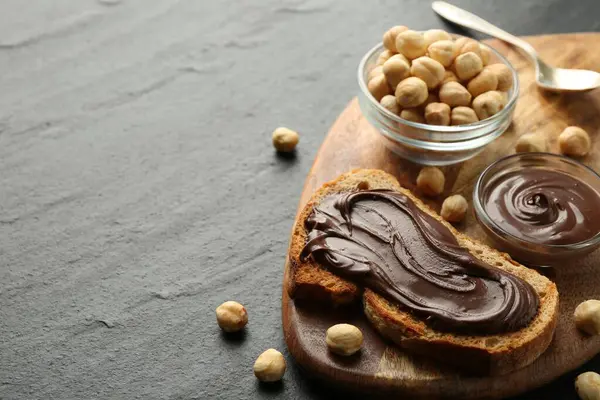 Çikolata sürülmüş bir dilim ekmek ve koyu dokulu masada fındıklar, yakın plan. Metin için boşluk