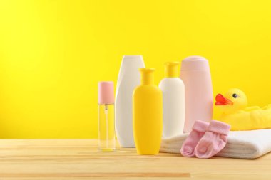 Bebek kozmetik ürünleri ve banyo aksesuarları ahşap masada, sarı arka planda. Metin için boşluk
