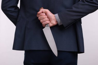 Beyaz arka planda sırtında bıçak tutan iş adamı, yakın plan.