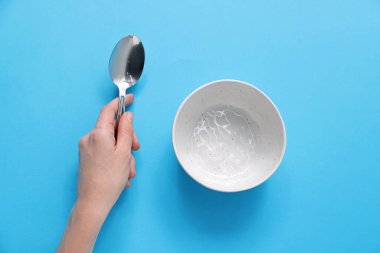 Kaşıklı ve boş kaseli bir kadın açık mavi arka planda, üst manzara