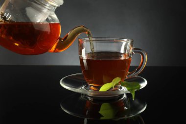 Çaydanlıktan taze demlenmiş çayı siyah masaya, cam fincana dökerek.