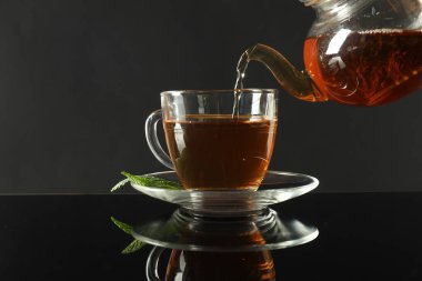 Koyu ayna masasında çaydanlıktan fincana taze demlenmiş çay dökülüyor.