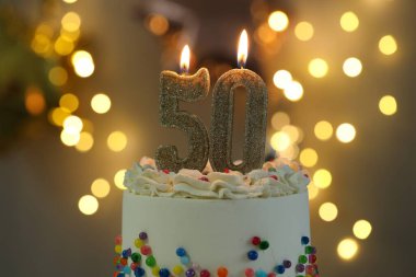 50th birthday. Burning number shaped candles on cake against blurred background with lights, closeup. Bokeh effect