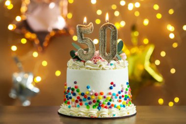 50. yaş günü. Yanan mumlar ve ahşap masaya serpiştirilmiş arkaplanda bulanık ışıklar ve bokeh efekti olan lezzetli bir pasta.