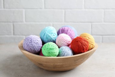 Balls of colorful yarn in bowl on light grey table, closeup