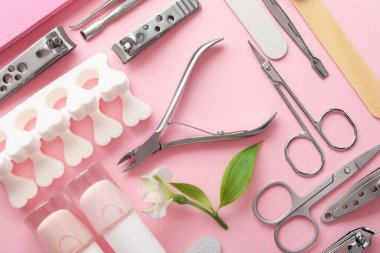 Pembe arka planda farklı manikür aletleri ve çiçek seti.