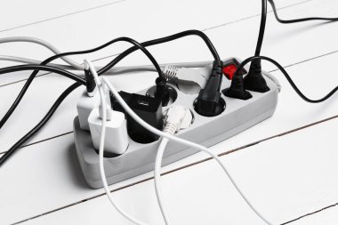 Eklenti güç panosu beyaz ahşap zeminde tıkaçlarla aşırı yüklenmiş, yakın plan.