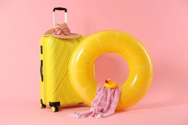 Sarı şişirilebilir yüzük, bavul ve pembe arka planda plaj aksesuarları.