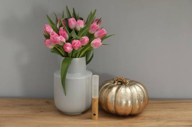 Vazoda güzel laleler, LED lamba ve ahşap masada süslü balkabağı, gri duvarın yanında.