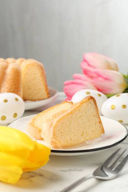 Lezzetli kek parçaları, Paskalya yumurtaları ve laleler açık mermer masada.