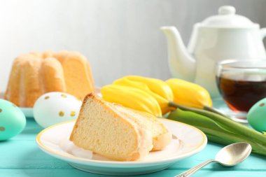 Lezzetli kek parçaları, Paskalya yumurtaları, laleler ve çay açık mavi ahşap masada, yakın plan.