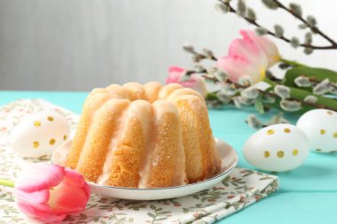 Lezzetli kek, Paskalya yumurtası, söğüt dalları ve açık mavi ahşap masada laleler.