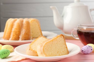 Lezzetli kek parçaları, pembe ahşap masada paskalya yumurtası ve çay.