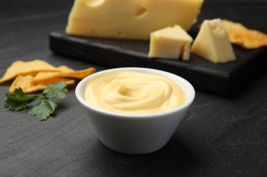 Peynir sosunu kaseye daldırmak, cips ve maydanozu siyah masaya koymak, yakın plan.