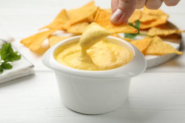 Beyaz ahşap masada lezzetli peynir sosuna cips bandıran kadın, yakın plan.