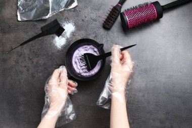 Kadın, gri arka planda saç beyazlatıcı karışımı yapıyor.