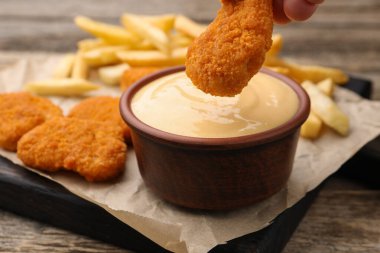 Ahşap masada tavuk parçalarını peynir sosuna batıran kadın, yakın plan.