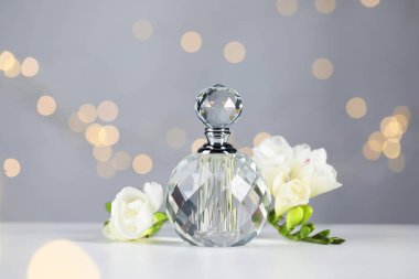 Bir şişe aromatik parfüm ve çiçek, arka plandaki gri ışıklara karşı, yakın plan. Bokeh etkisi