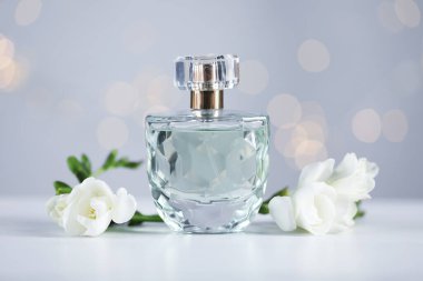 Bir şişe aromatik parfüm ve çiçek, arka plandaki gri ışıklara karşı, yakın plan. Bokeh etkisi